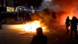 Varios manifestantes encapuchados desafían a las fuerzas del orden tras incendiar un contenedor de basura en Róterdam.