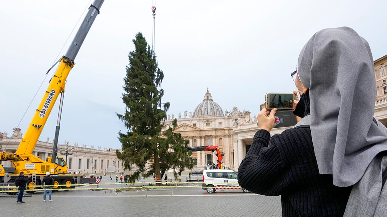A nun takes photos as a crane lifts a 113-year-old and 28-meter-tall spruce in St. Peter's Square, to serve as a Christmas tree, at the Vatican