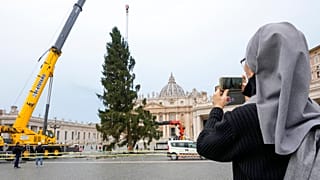 A nun takes photos as a crane lifts a 113-year-old and 28-meter-tall spruce in St. Peter's Square, to serve as a Christmas tree, at the Vatican