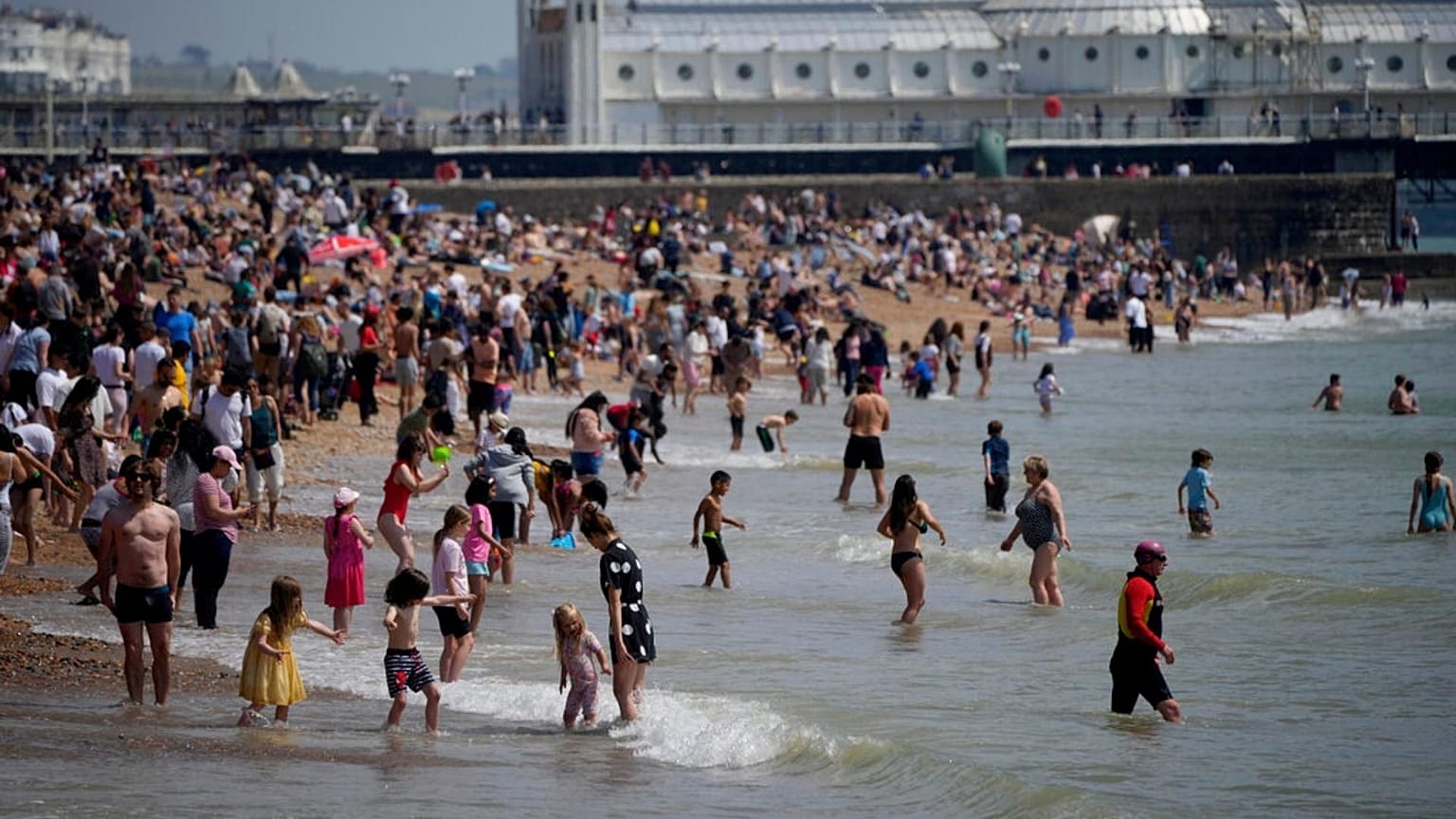People venture into the sea as they enjoy themselves during a hot day on Brighton Beach.