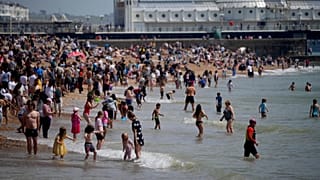 People venture into the sea as they enjoy themselves during a hot day on Brighton Beach.