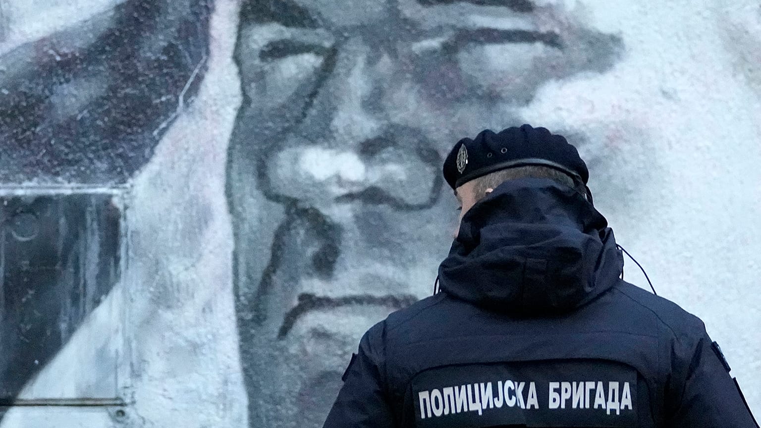 A police officer stands by a mural of former Bosnian Serb military chief Ratko Mladić in Belgrade, Serbia, Tuesday, Nov. 9, 2021.