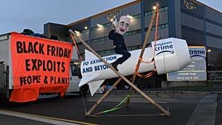 An activist dressed as Jeff Bezos rides a rocket outside of an Amazon depot. 