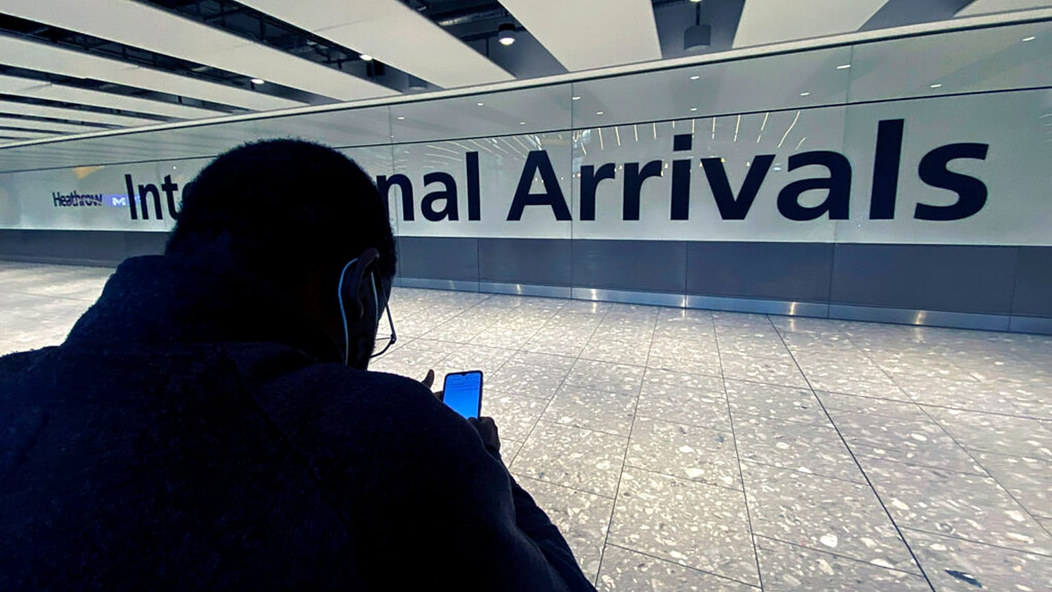 Un hombre consulta su teléfono móvil en la sección de llegadas del aeropuerto internacional de Heathrow, en Londres, el viernes 26 de noviembre de 2021.