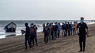 مهاجرون من المغرب يسيرون على طول الشاطئ برفقة الشرطة الإسبانية بعد وصولهم إلى ساحل جزيرة الكناري، الثلاثاء 20 أكتوبر/تشرين الأول 2020