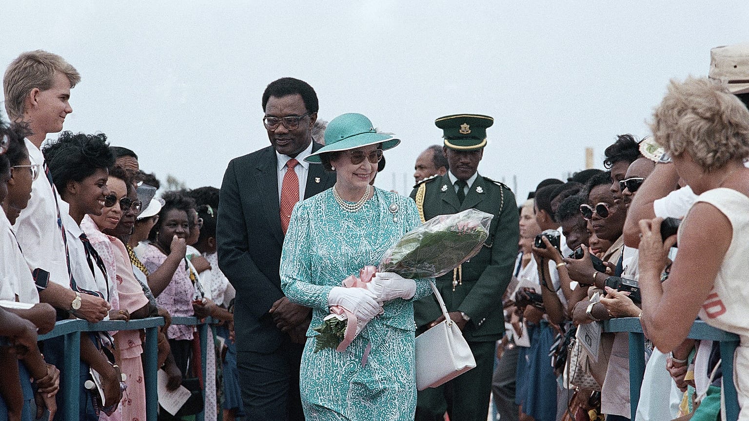 Barbadians line both sides of a red carpet as British Queen Elizabeth II carries flowers presented to her on Friday, March 10, 1989 at Queen's College in Barbados.