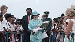 Barbadians line both sides of a red carpet as British Queen Elizabeth II carries flowers presented to her on Friday, March 10, 1989 at Queen's College in Barbados.