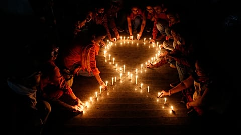 Members of a NGO make a red ribbon, the universal symbol of awareness and support for those living with HIV, with candles on the eve of World AIDS day in India, Nov. 30, 2021.