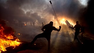 دخان أسود في السماء مع قيام متظاهرين فلسطينيين بإلقاء الحجارة على القوات الإسرائيلية خلال مظاهرة على حدود قطاع غزة مع إسرائيل