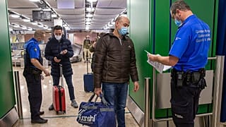 Zwei Grenzbeamte lassen sich am Flughafen Genf von Reisenden die Papiere zeigen (Aufnahmen vom Februar 2021)