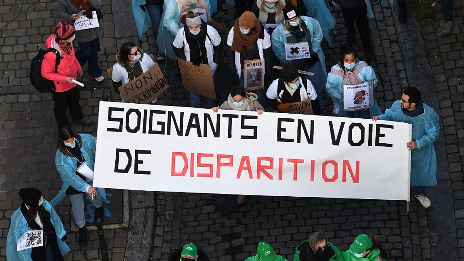 Health care workers hold a banner which reads as "Endangered caregivers" 