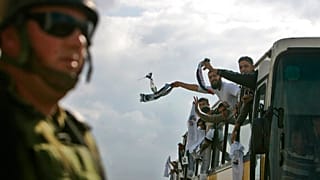 جندي إسرائيلي يشاهد أسرى فلسطينيين أطلق سراحهم يحتفلون بعد عبورهم حاجز بيتونيا العسكري إلى مدينة رام الله بالضفة الغربية، الإثنين 15 ديسمبر 2008