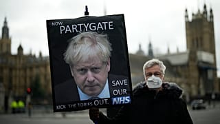 An anti-Conservative Party protester holds a placard with an image of British PM Boris Johnson including the words "Partygate" in London, Wednesday, Dec. 8, 2021.