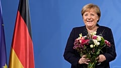 Former Chancellor Angela Merkel laughs as she receives flowers from new elected Chancellor Olaf Scholz during a handover ceremony in the chancellery in Berlin, Dec. 8, 2021.