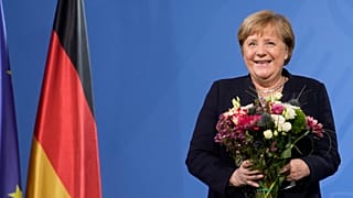 Former Chancellor Angela Merkel laughs as she receives flowers from new elected Chancellor Olaf Scholz during a handover ceremony in the chancellery in Berlin, Dec. 8, 2021.