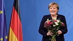 The former Chancellor laughs as she receives flowers from the newly elected Olaf Scholz during a handover ceremony