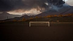 Un campo de fútbol está cubierto por cenizas negras mientras la lava fluye desde el volcán, en la isla canaria de La Palma, España, el lunes 6 de diciembre de 2021