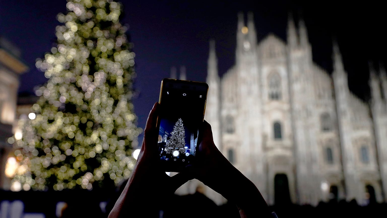 A woman takes pictures of the lit Christmas tree in front of the Duomo gothic cathedral, in Milan, Italy, Sunday, Dec. 16, 2018