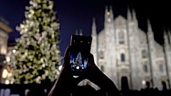 A woman takes pictures of the lit Christmas tree in front of the Duomo gothic cathedral, in Milan, Italy, Sunday, Dec. 16, 2018
