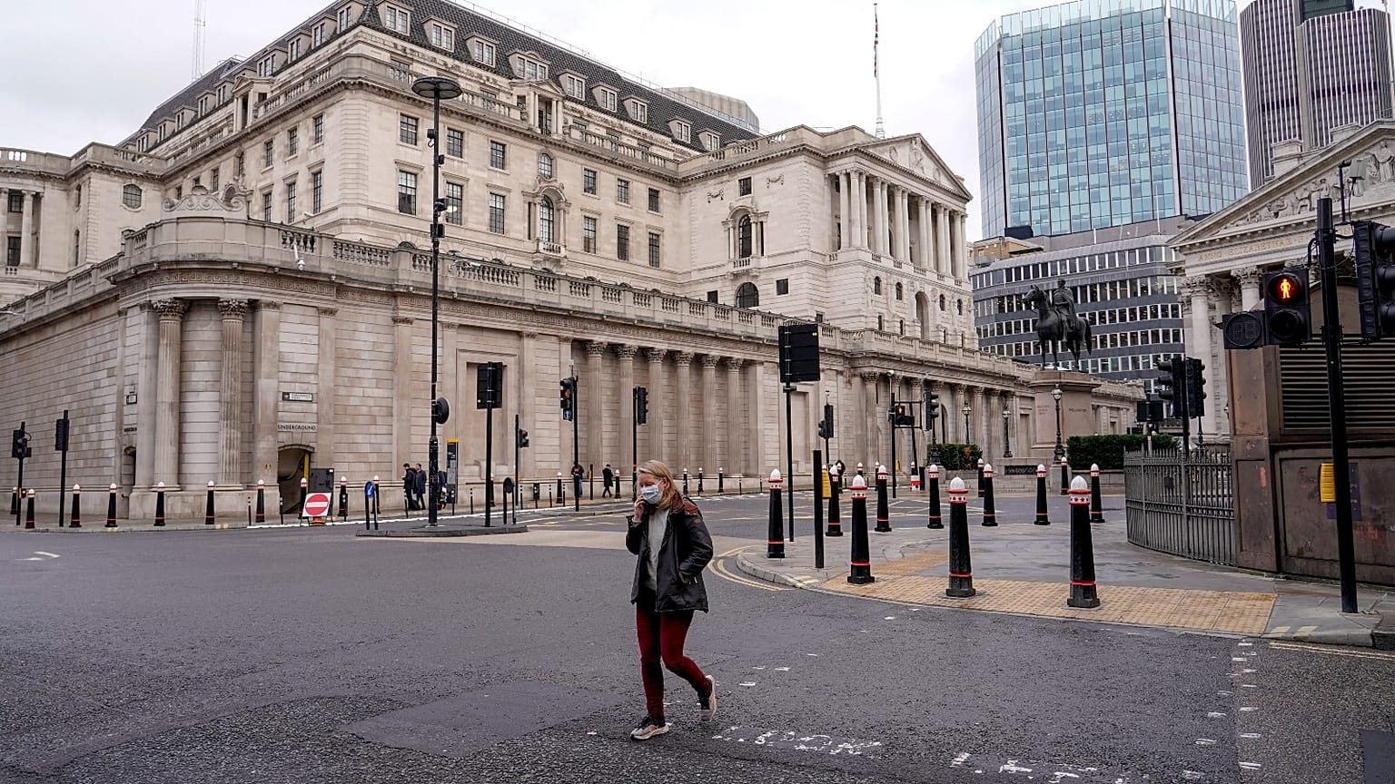 FILE - A woman wears a face mask while walking crossing a road outside the Bank of England, in the financial district, known as The City, in London, Monday, Dec. 13, 2021.
