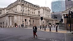 FILE - A woman wears a face mask while walking crossing a road outside the Bank of England, in the financial district, known as The City, in London, Monday, Dec. 13, 2021.