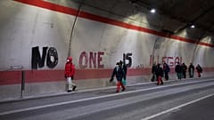 Migrants headed to France from Italy walk past graffiti that reads "No One is Illegal" in a tunnel leading to the French-Italian border, Saturday, Dec. 11, 2021.