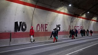 Migrants headed to France from Italy walk past graffiti that reads "No One is Illegal" in a tunnel leading to the French-Italian border, Saturday, Dec. 11, 2021.
