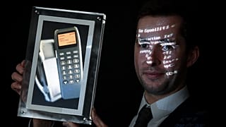 Maximillien Aguttes, de la maison de vente aux enchères Aguttes, présente un écran montrant un téléphone avec le tout premier SMS au monde