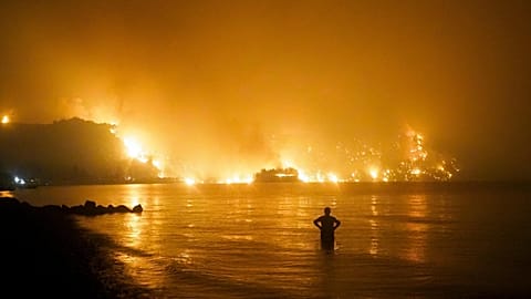 A man watches as a wildfire approaches Kochyli beach near the village of Limni, Greece, about 160 kilometers (100 miles) north of Athens, on Aug. 6, 2021.