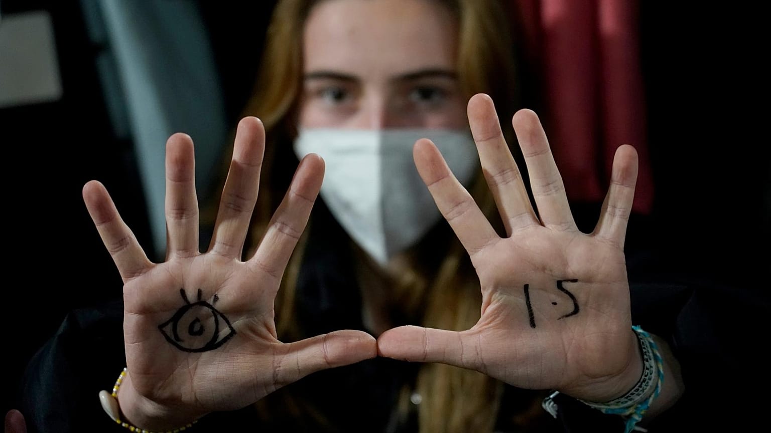A young woman with an eye drawn on her hand to show she is watching and 1.5 for countries to keep warming below 1.5 degrees Celsius.