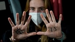 A young woman with an eye drawn on her hand to show she is watching and 1.5 for countries to keep warming below 1.5 degrees Celsius.