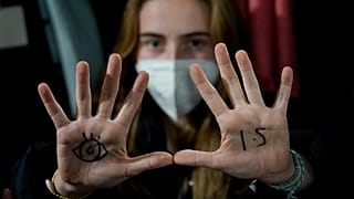 A young woman with an eye drawn on her hand to show she is watching and 1.5 for countries to keep warming below 1.5 degrees Celsius.
