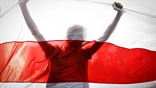 Demonstrator is silhouetted by an old Belarusian national flag during a rally in Minsk, Belarus, Sunday, Oct. 4, 2020