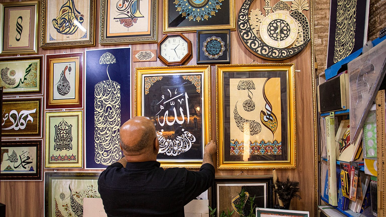 الخطاط العراقي وائل رمضان يعلق إحدى قطعه الفنية المؤطرة بالخط العربي، مكتوب عليها "الله" بأسلوب خط الثلث في محله بحي العشار بمدينة البصرة جنوب العراق.