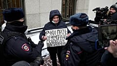 Police officers detain a demonstrator holding a poster reading "Hands off the Memorial, freedom for political prisoners" as other people gather in front of the Supreme Court