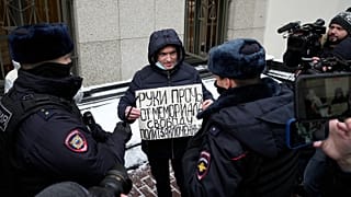 Police officers detain a demonstrator holding a poster reading "Hands off the Memorial, freedom for political prisoners" as other people gather in front of the Supreme Court