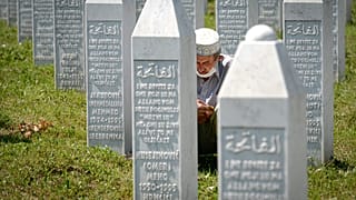 رجل يصلي جالسًا بين حجارة القبور في بوتوكاري بالقرب من سريبرينيتشا - البوسنة. 2020/07/11