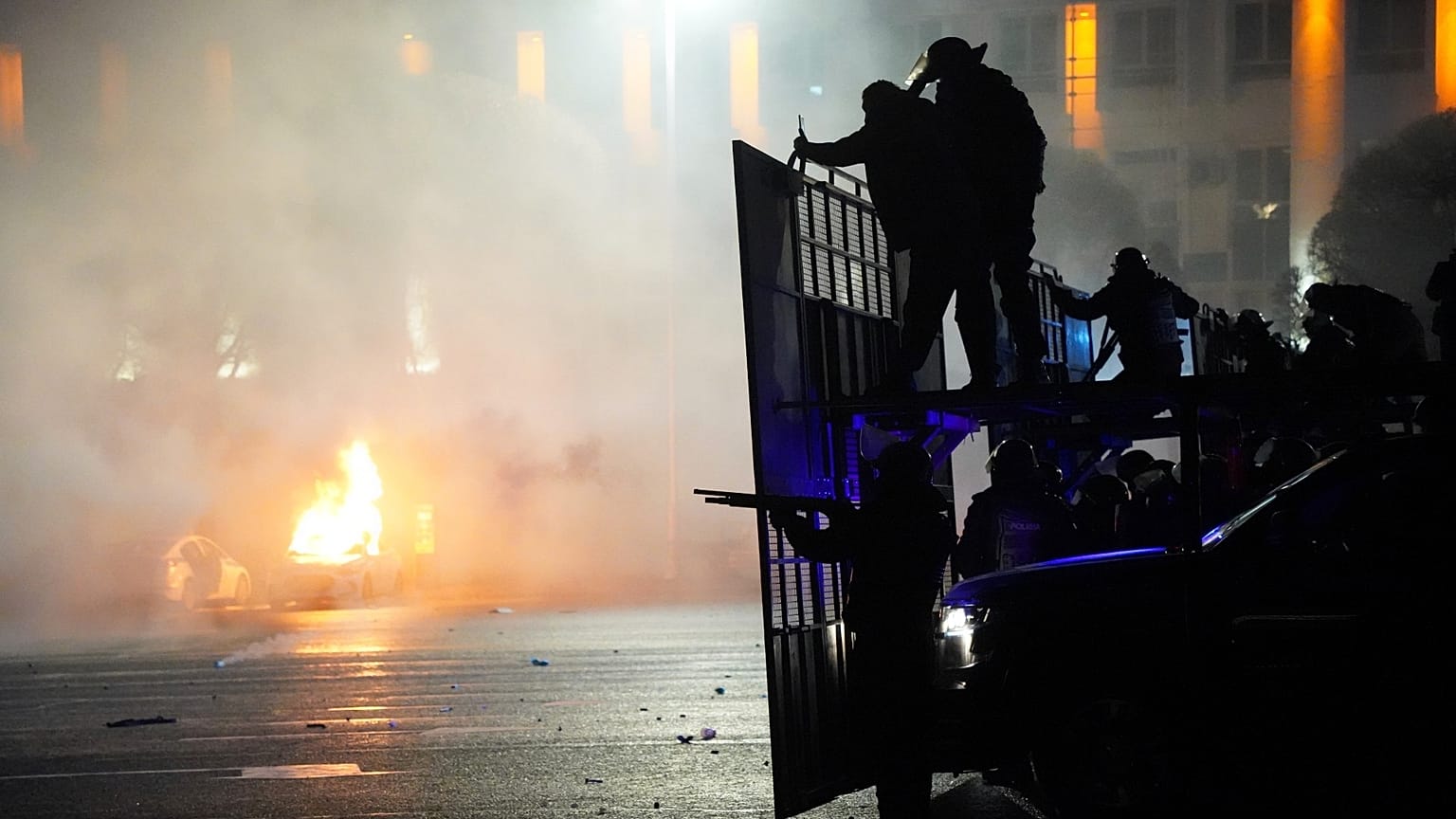 A police car on fire as riot police prepare to stop protesters in the center of Almaty, Kazakhstan, Jan. 5, 2022. 