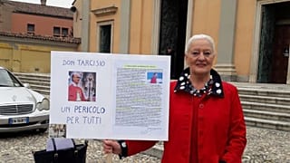 Silvia de Martini stands outside a church in Casorate Primo with a placard denouncing FatherTarcisio Colombo. It reads: "Don Tarcisio, a danger for everyone".