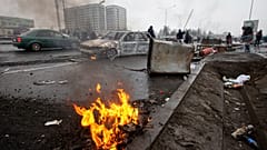 People walk past cars, which were burned after clashes, on a street in Almaty, Kazakhstan, Friday, Jan. 7, 2022.