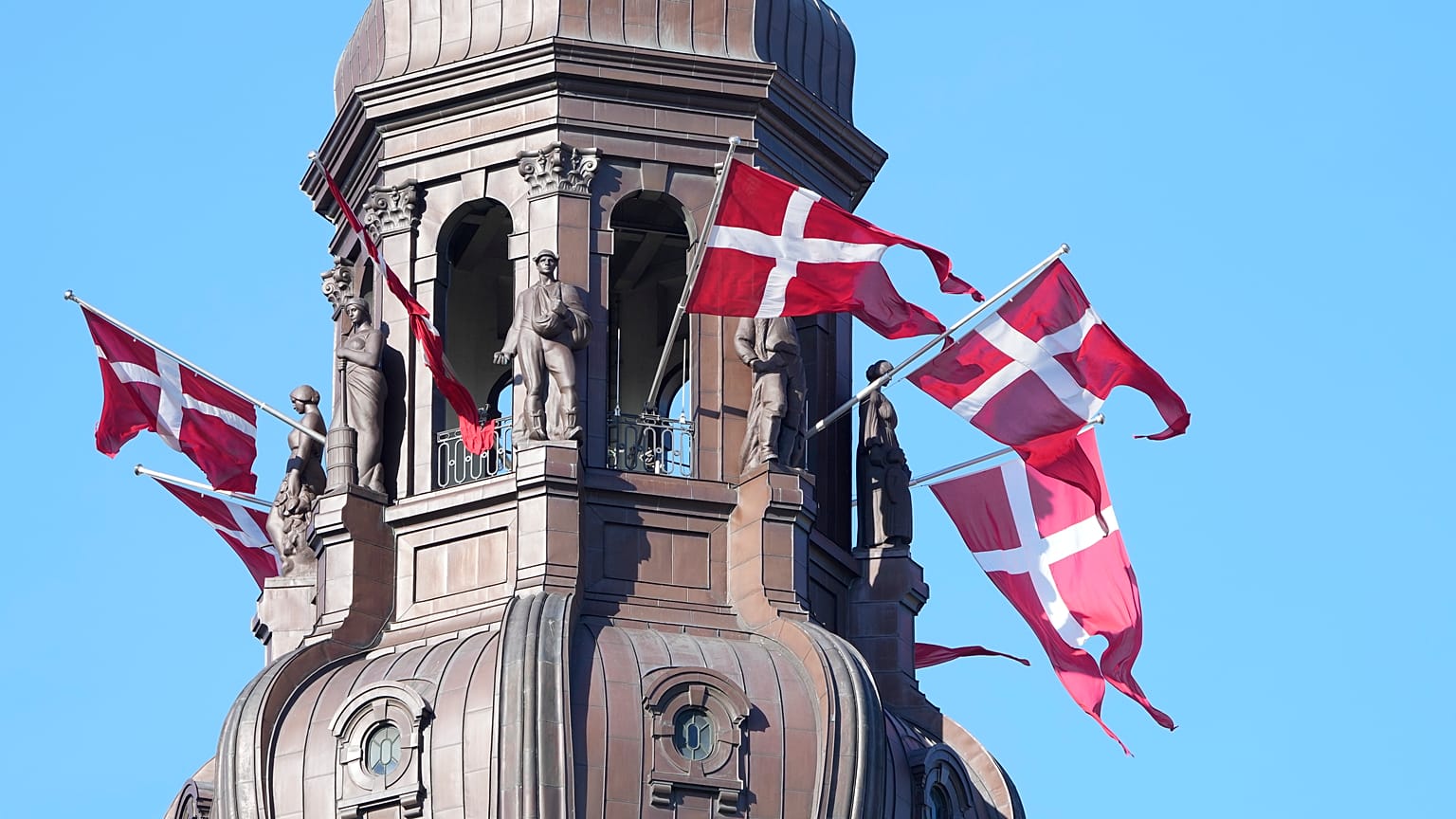 Danish flags are attached to the spire of the Danish Parliament building in Copenhagen.