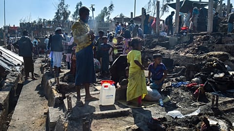 People gather on the ground of brunt-out houses after a fire gutted parts of a Rohingya refugee camp.