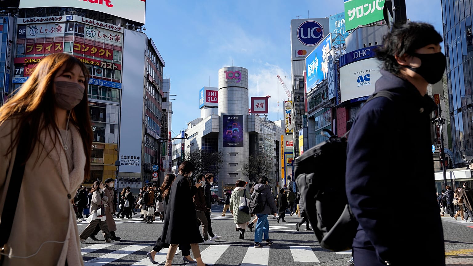 People wearing protective masks to help curb the spread of the coronavirus walk along a pedestrian crossing on Friday, Jan. 21, 2022, in Tokyo.