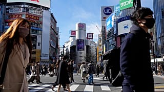 People wearing protective masks to help curb the spread of the coronavirus walk along a pedestrian crossing on Friday, Jan. 21, 2022, in Tokyo.