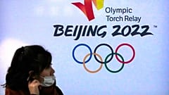 امرأة ترتدي قناعًا للوجه تمر بالقرب من شعار أولمبياد بكين الشتوى 2022