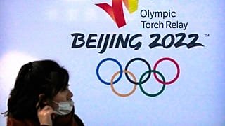 امرأة ترتدي قناعًا للوجه تمر بالقرب من شعار أولمبياد بكين الشتوى 2022