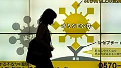 Japán nő sétál el a Tokió egyik aluljárójában elhelyezett, a koronavírusról szóló ismertetők előtt