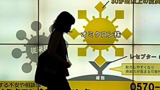 Japán nő sétál el a Tokió egyik aluljárójában elhelyezett, a koronavírusról szóló ismertetők előtt