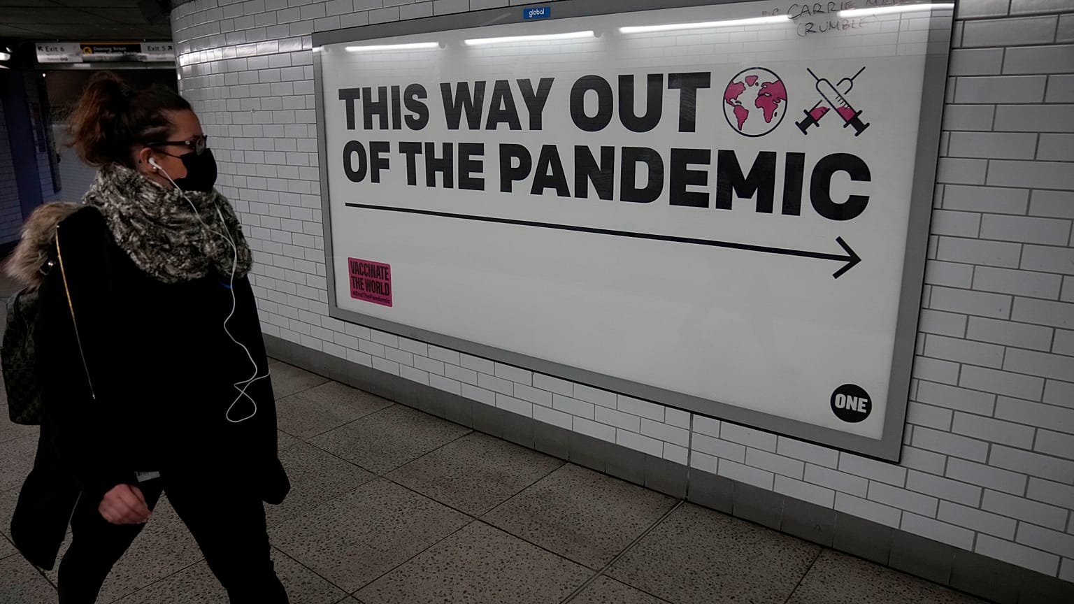 A woman walks past a health campaign poster from the One NGO, in an underpass leading to Westminster underground train station, in London, Thursday, Jan. 27, 2022. 