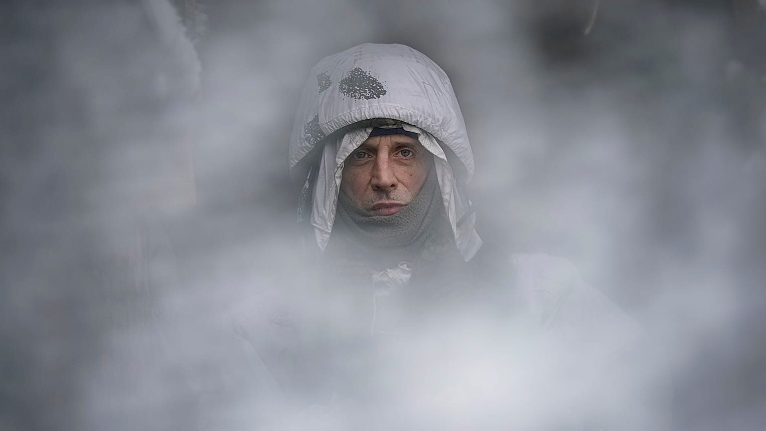 A Ukrainian serviceman, seen through a camouflage mesh, stands at a frontline position in the Luhansk region, eastern Ukraine